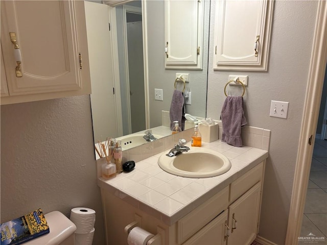 half bathroom featuring a textured wall, toilet, tile patterned floors, and vanity