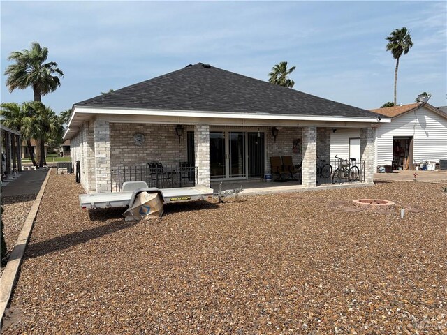 rear view of house featuring brick siding, a fire pit, roof with shingles, and a patio area
