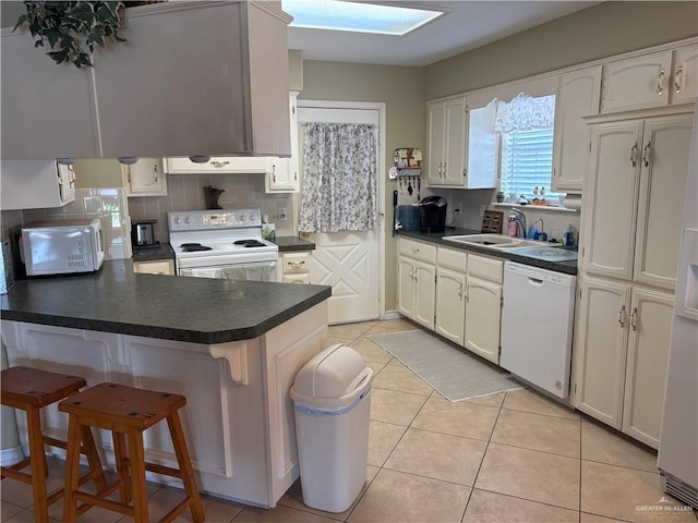 kitchen with white appliances, dark countertops, a sink, and a peninsula