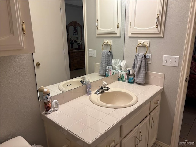 bathroom featuring toilet, vanity, and a textured wall
