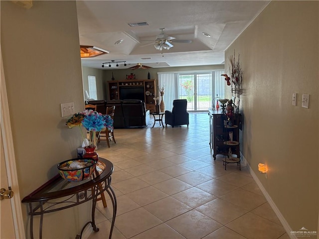 interior space with a raised ceiling, light tile patterned floors, baseboards, visible vents, and ceiling fan