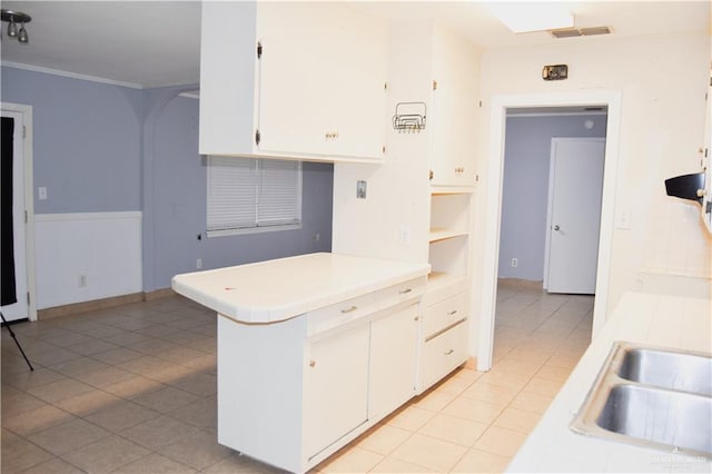 kitchen featuring kitchen peninsula, crown molding, sink, light tile patterned floors, and white cabinetry