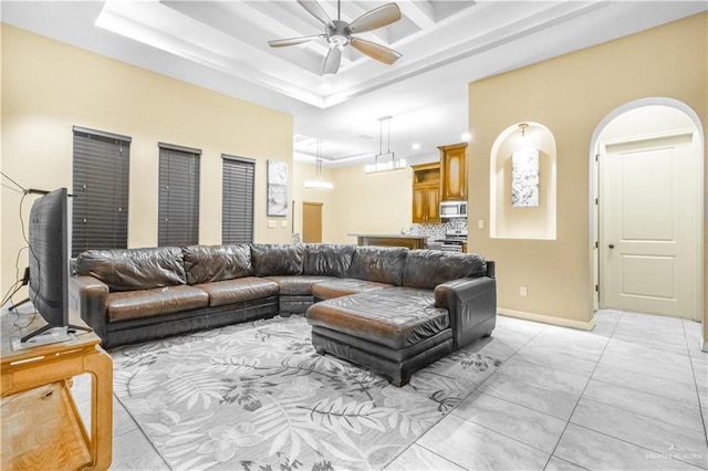 living room with a tray ceiling, ceiling fan, and light tile patterned flooring