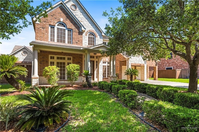 traditional-style house featuring concrete driveway, a front lawn, stone siding, fence, and brick siding