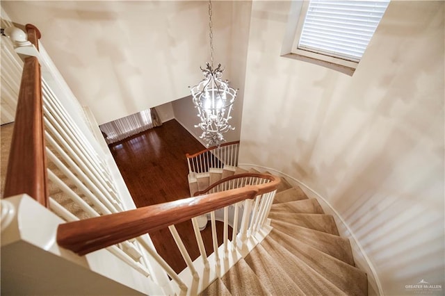 stairway with wood finished floors and an inviting chandelier