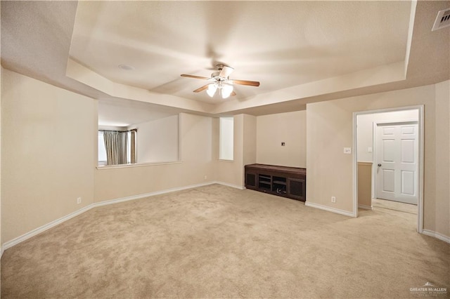 unfurnished living room featuring a raised ceiling, light carpet, and ceiling fan