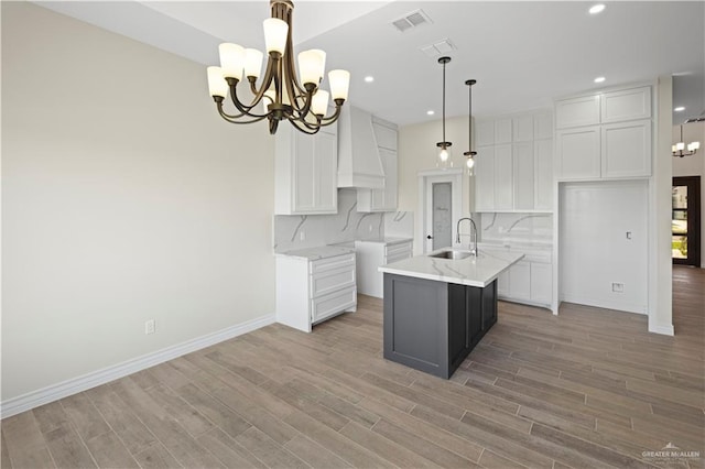 kitchen featuring sink, tasteful backsplash, a center island with sink, pendant lighting, and white cabinets