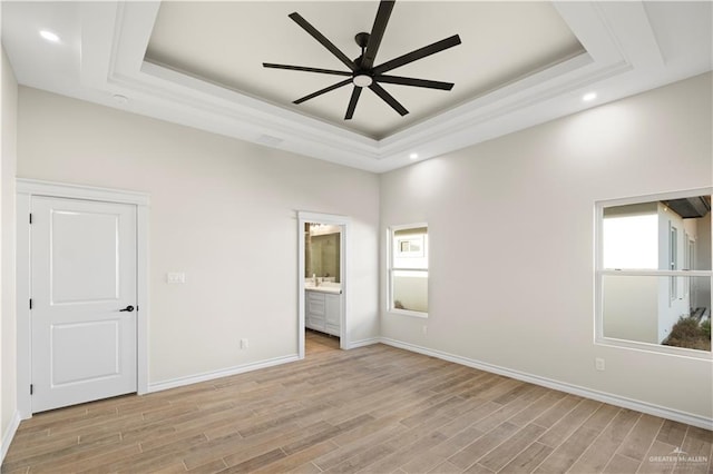 unfurnished bedroom with ensuite bath, light hardwood / wood-style flooring, and a raised ceiling