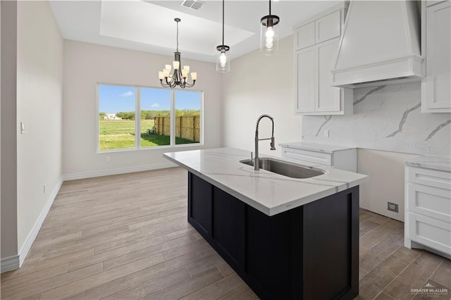 kitchen with sink, decorative light fixtures, an island with sink, and white cabinets