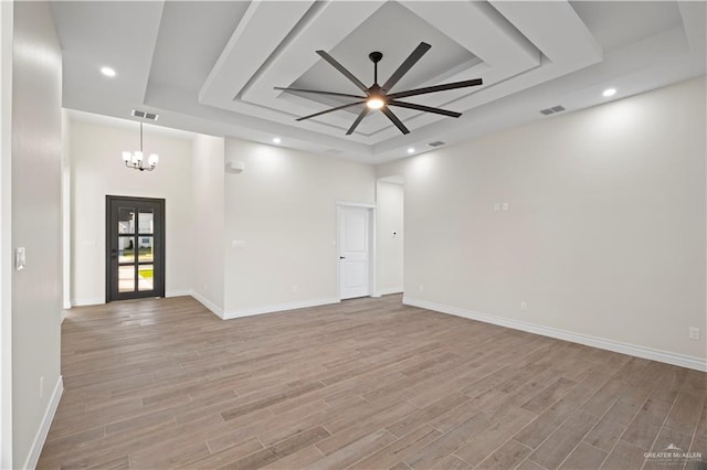 unfurnished room featuring a raised ceiling, ceiling fan with notable chandelier, and light wood-type flooring