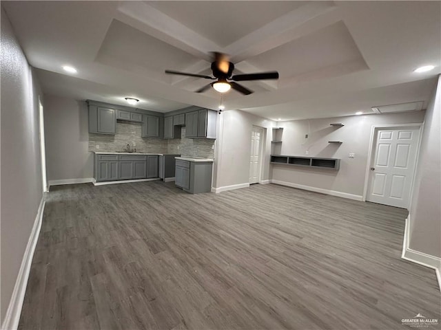 kitchen with backsplash, dark wood-type flooring, a raised ceiling, ceiling fan, and gray cabinets