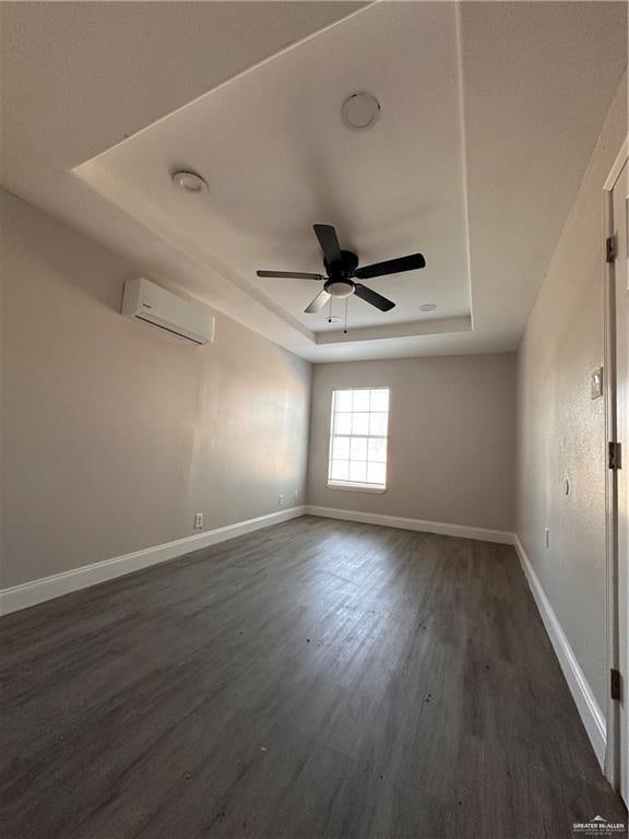 spare room featuring dark hardwood / wood-style flooring, a tray ceiling, a wall mounted AC, and ceiling fan