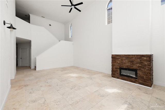 unfurnished living room featuring ceiling fan, a fireplace, and a towering ceiling