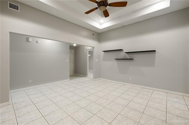 unfurnished room with ceiling fan, a tray ceiling, visible vents, and baseboards