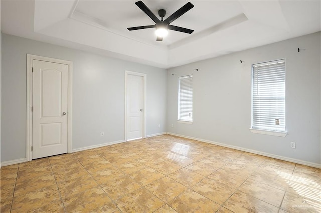 unfurnished room featuring a wealth of natural light, a tray ceiling, and baseboards