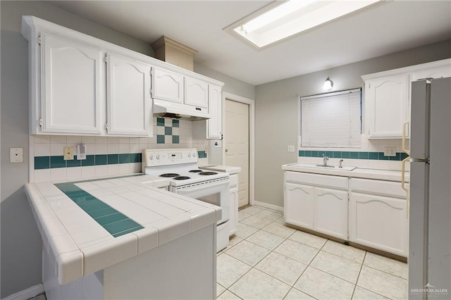 kitchen featuring white appliances, tile counters, under cabinet range hood, white cabinetry, and a sink