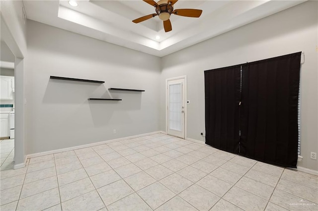 foyer with light tile patterned floors, baseboards, a tray ceiling, and a ceiling fan