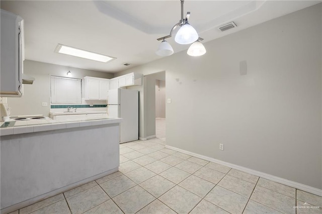 kitchen with tile counters, visible vents, freestanding refrigerator, a sink, and a peninsula