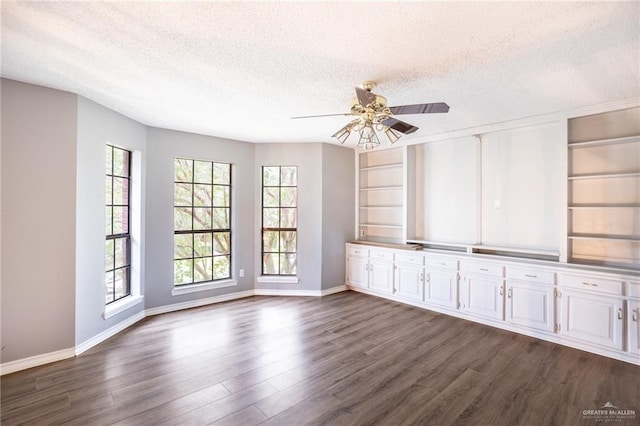 empty room with a textured ceiling, dark hardwood / wood-style flooring, ceiling fan, and built in shelves