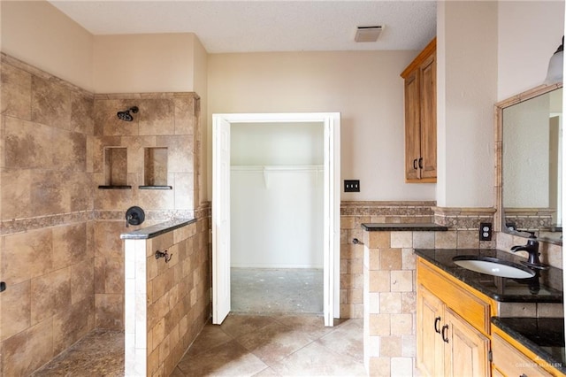 bathroom with tiled shower, vanity, tile patterned floors, and tile walls