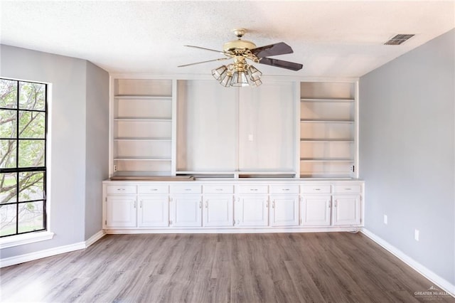 unfurnished living room with built in features, light hardwood / wood-style flooring, ceiling fan, and a textured ceiling