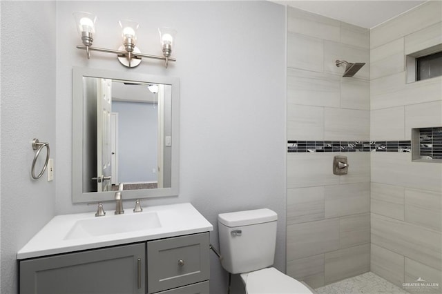 bathroom featuring a tile shower, toilet, and vanity