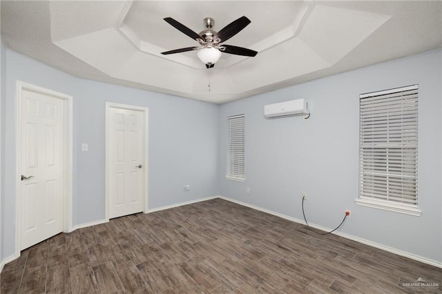 empty room featuring a raised ceiling, baseboards, dark wood-style flooring, and a wall mounted air conditioner