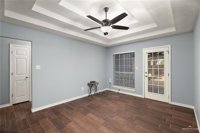 empty room featuring a ceiling fan, baseboards, wood finish floors, a tray ceiling, and a textured ceiling