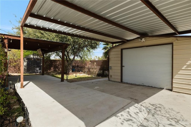 view of patio / terrace featuring fence, a garage, an outdoor structure, a carport, and driveway