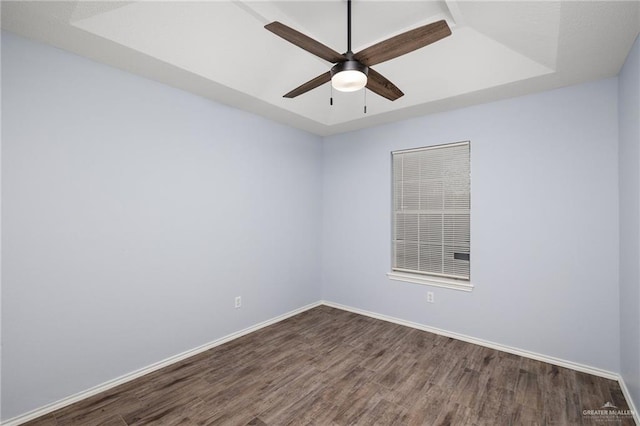 empty room with baseboards, a raised ceiling, dark wood-type flooring, and a ceiling fan