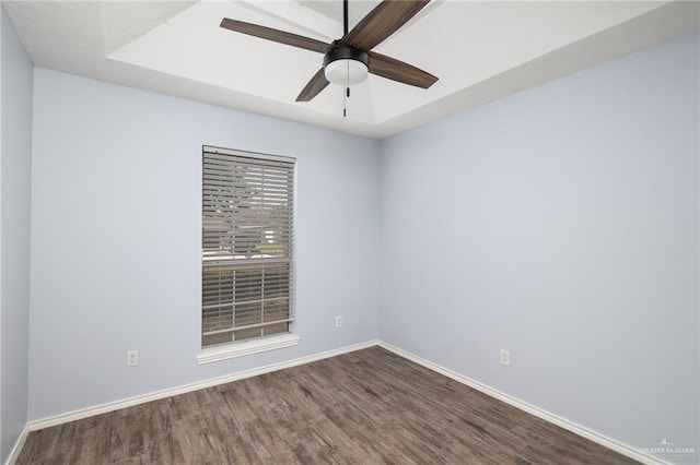 empty room with ceiling fan, baseboards, a raised ceiling, and dark wood-style floors