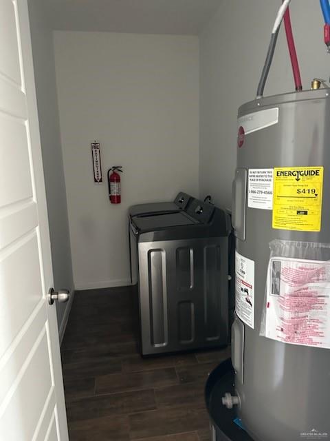 clothes washing area with washing machine and clothes dryer, electric water heater, and dark hardwood / wood-style floors