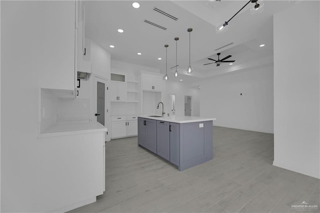 kitchen with sink, hanging light fixtures, an island with sink, light hardwood / wood-style floors, and white cabinets