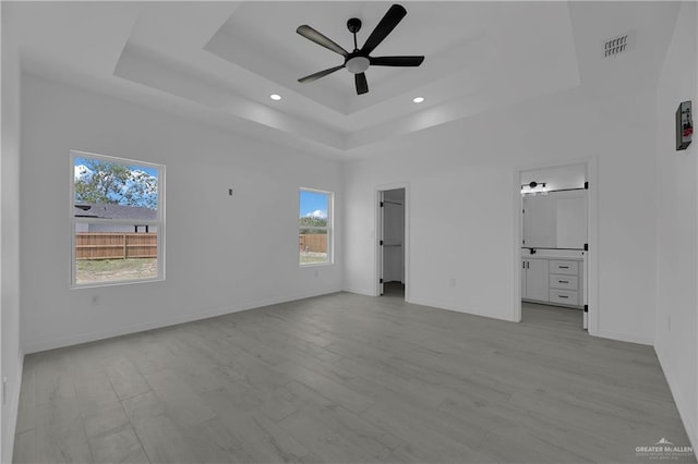 unfurnished bedroom with ceiling fan, light hardwood / wood-style flooring, connected bathroom, and a tray ceiling