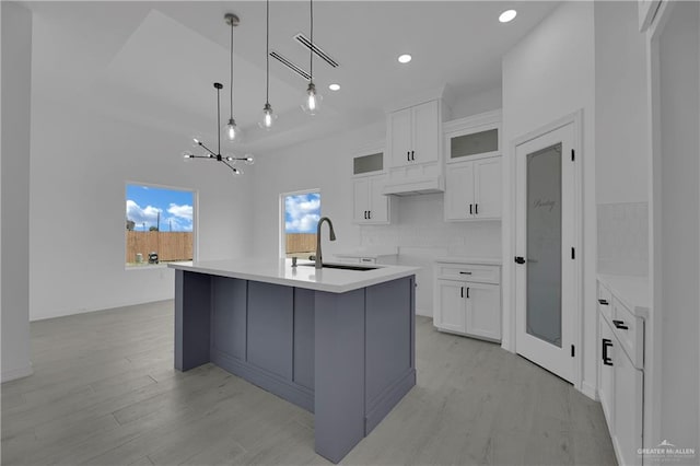 kitchen with an inviting chandelier, white cabinets, sink, an island with sink, and decorative light fixtures