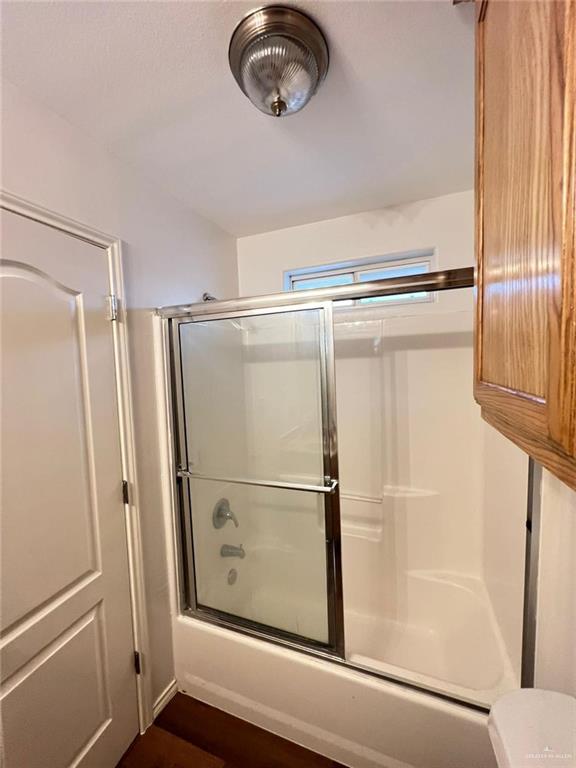 bathroom featuring hardwood / wood-style floors, toilet, and bath / shower combo with glass door