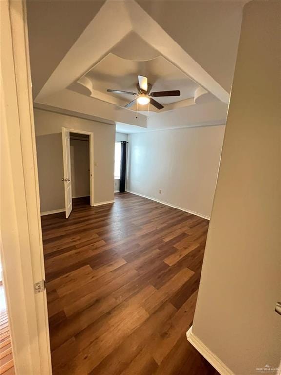 unfurnished room featuring a raised ceiling, ceiling fan, and dark wood-type flooring