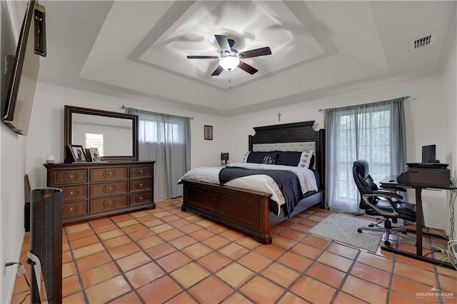 tiled bedroom with ceiling fan, a tray ceiling, and multiple windows