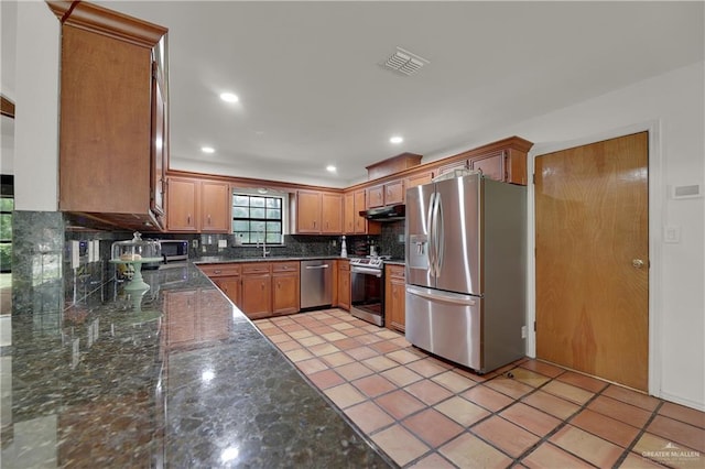 kitchen with light tile patterned floors, backsplash, stainless steel appliances, and dark stone counters