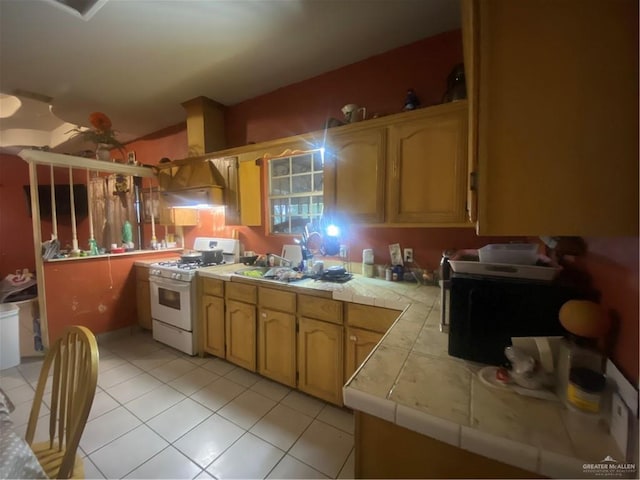 kitchen with tile counters, light tile patterned floors, and white gas range oven