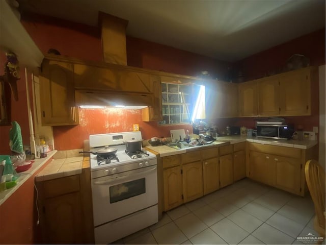 kitchen featuring gas range gas stove, custom range hood, sink, light tile patterned floors, and tile countertops