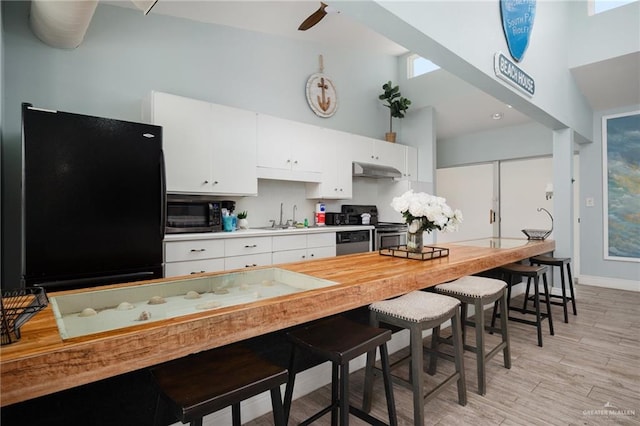 kitchen featuring a towering ceiling, light hardwood / wood-style floors, a breakfast bar area, white cabinets, and appliances with stainless steel finishes