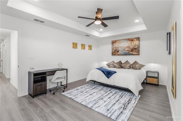 bedroom featuring ceiling fan, a tray ceiling, and light hardwood / wood-style flooring