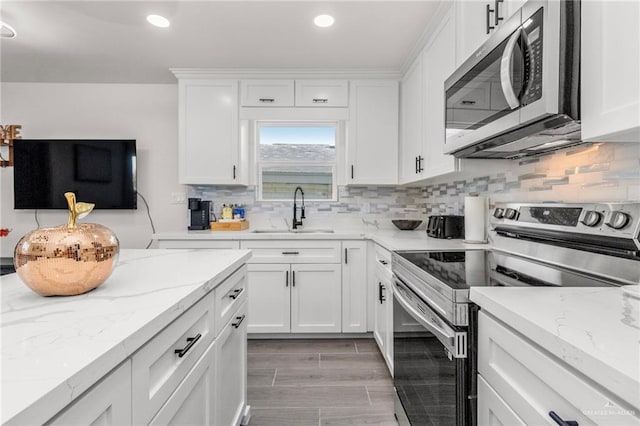 kitchen with stainless steel appliances, sink, white cabinets, and light stone counters