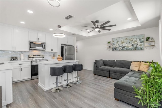 kitchen with decorative light fixtures, a center island, appliances with stainless steel finishes, a tray ceiling, and white cabinets