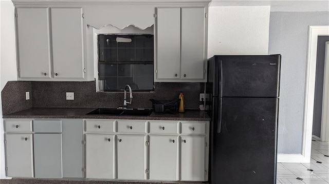 kitchen with black fridge, backsplash, white cabinetry, and sink