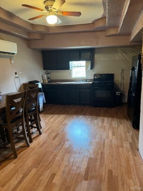 kitchen with black gas range, ceiling fan, sink, light hardwood / wood-style flooring, and an AC wall unit