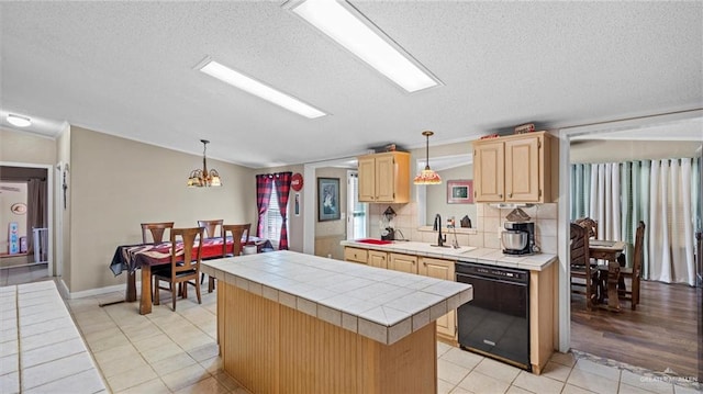 kitchen with pendant lighting, sink, black dishwasher, tile counters, and a kitchen island