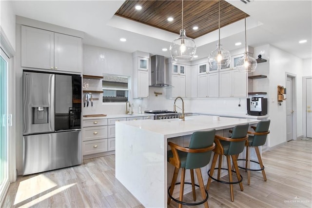 kitchen featuring light wood-style flooring, stainless steel fridge, wall chimney range hood, open shelves, and a raised ceiling