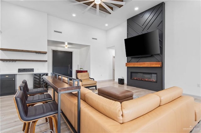 living room with recessed lighting, a high ceiling, light wood finished floors, and a large fireplace